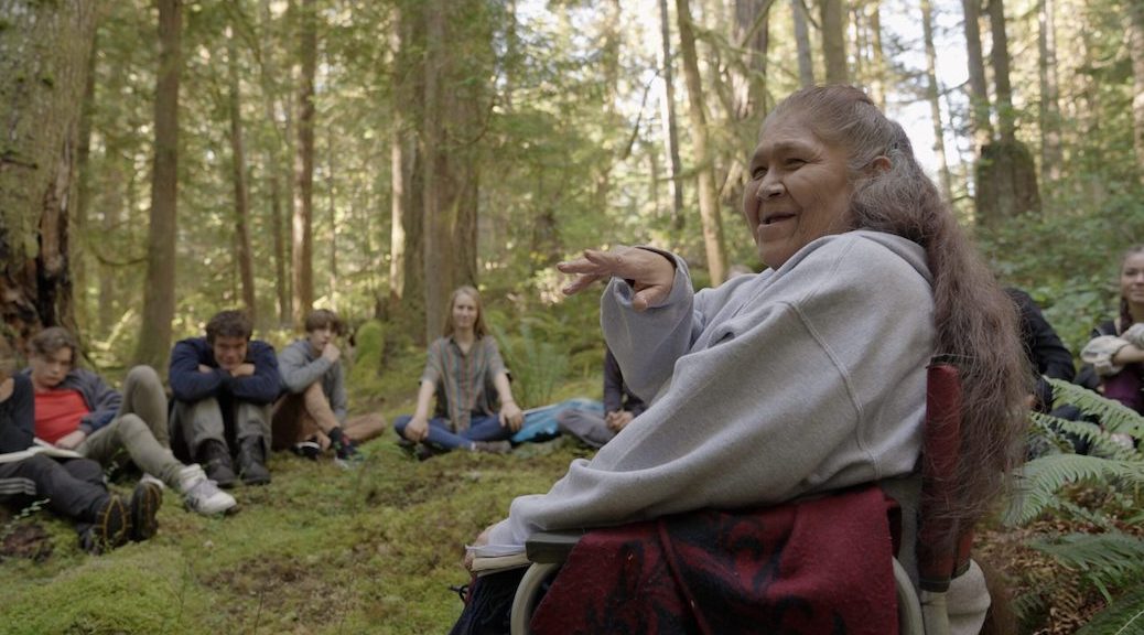An indigenous woman laughing as she speaks to students in the forest